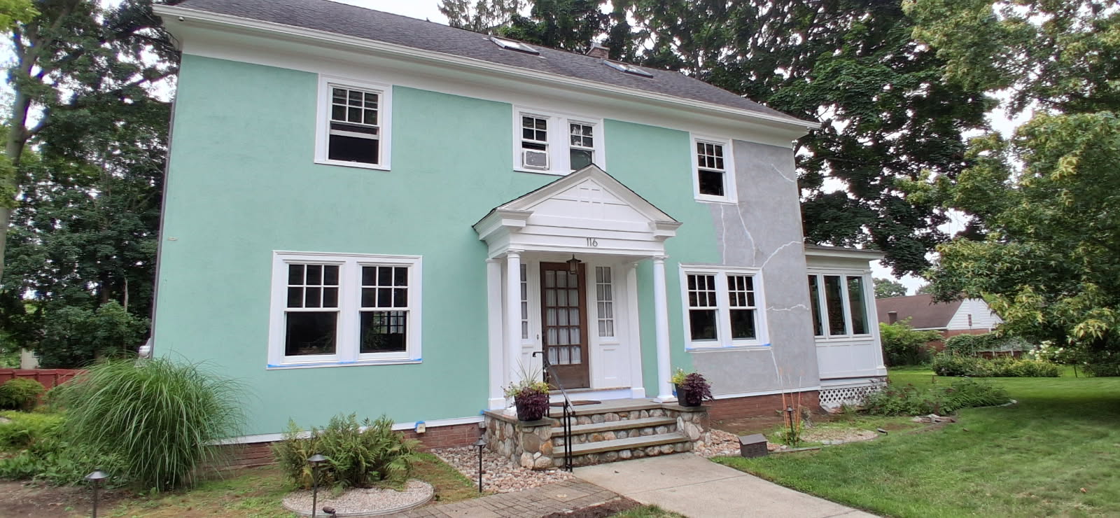Connecticut colonial home before painting, with mismatched mint stucco and patched grey repairs