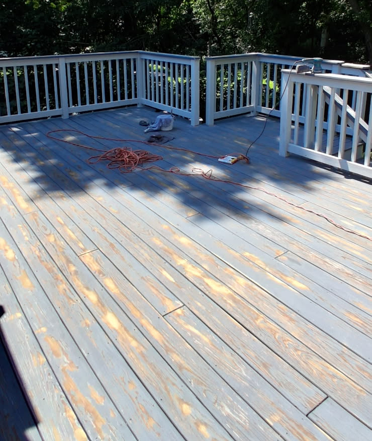 Weathered backyard deck with peeling grey stain and bare wood showing through the boards