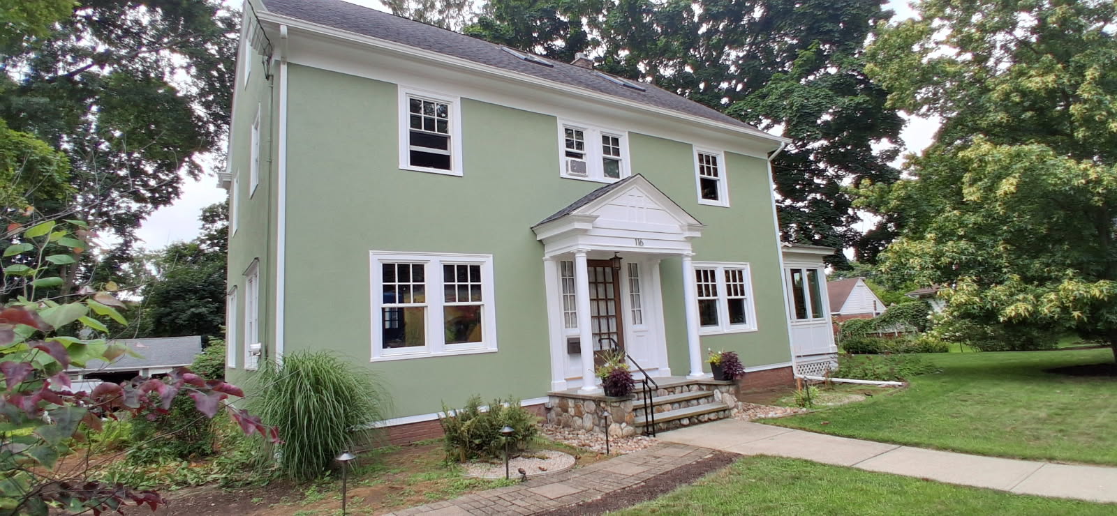 The same colonial home after a full exterior repaint in soft sage green with crisp white trim
